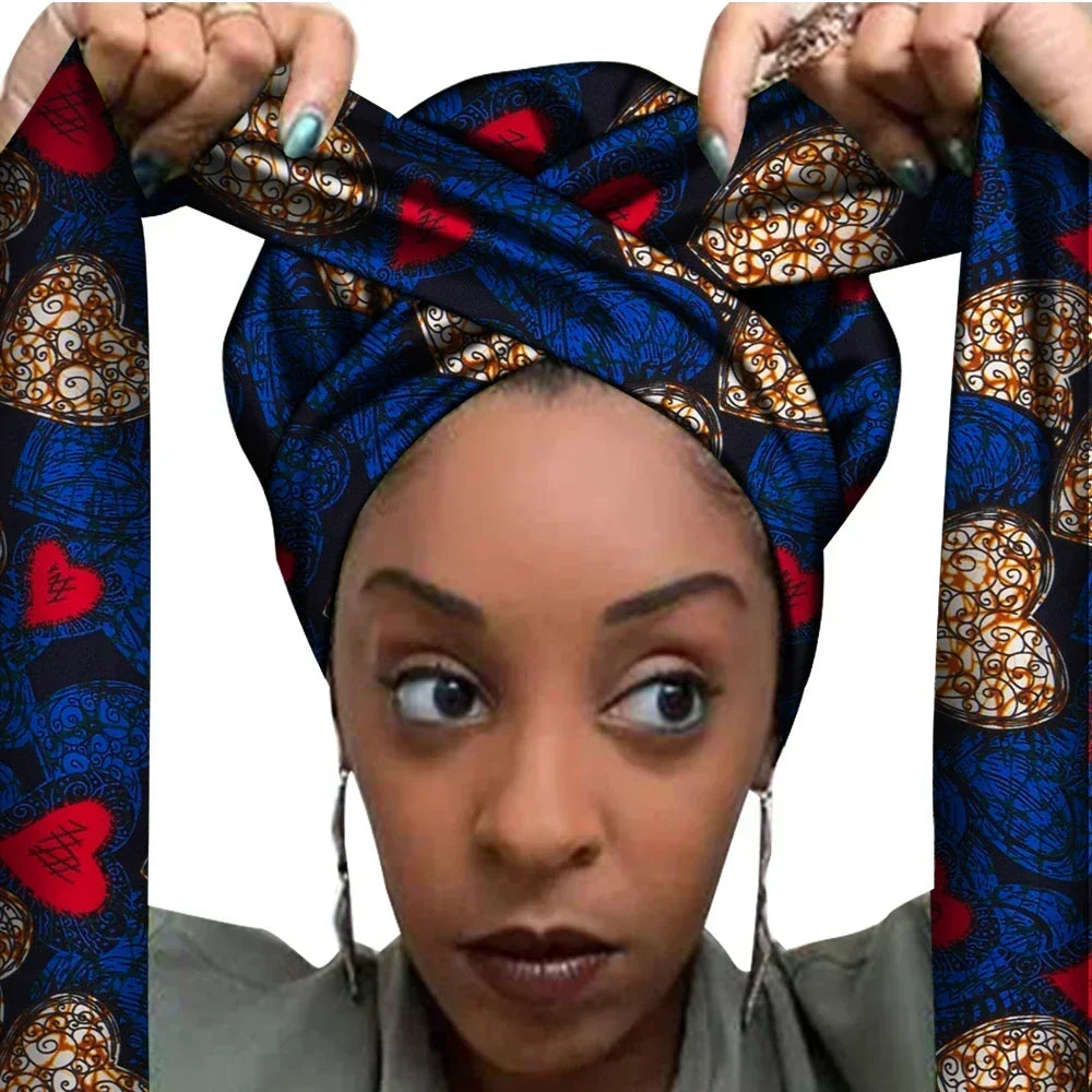 Vrouw met een Afrikaanse headwrap in donkerblauw, rood en goud Ankara print. De stof heeft een hartvormig patroon met sierlijke lijnen en accenten, lange linten en is handgemaakt van katoen, perfect voor lente en zomer.