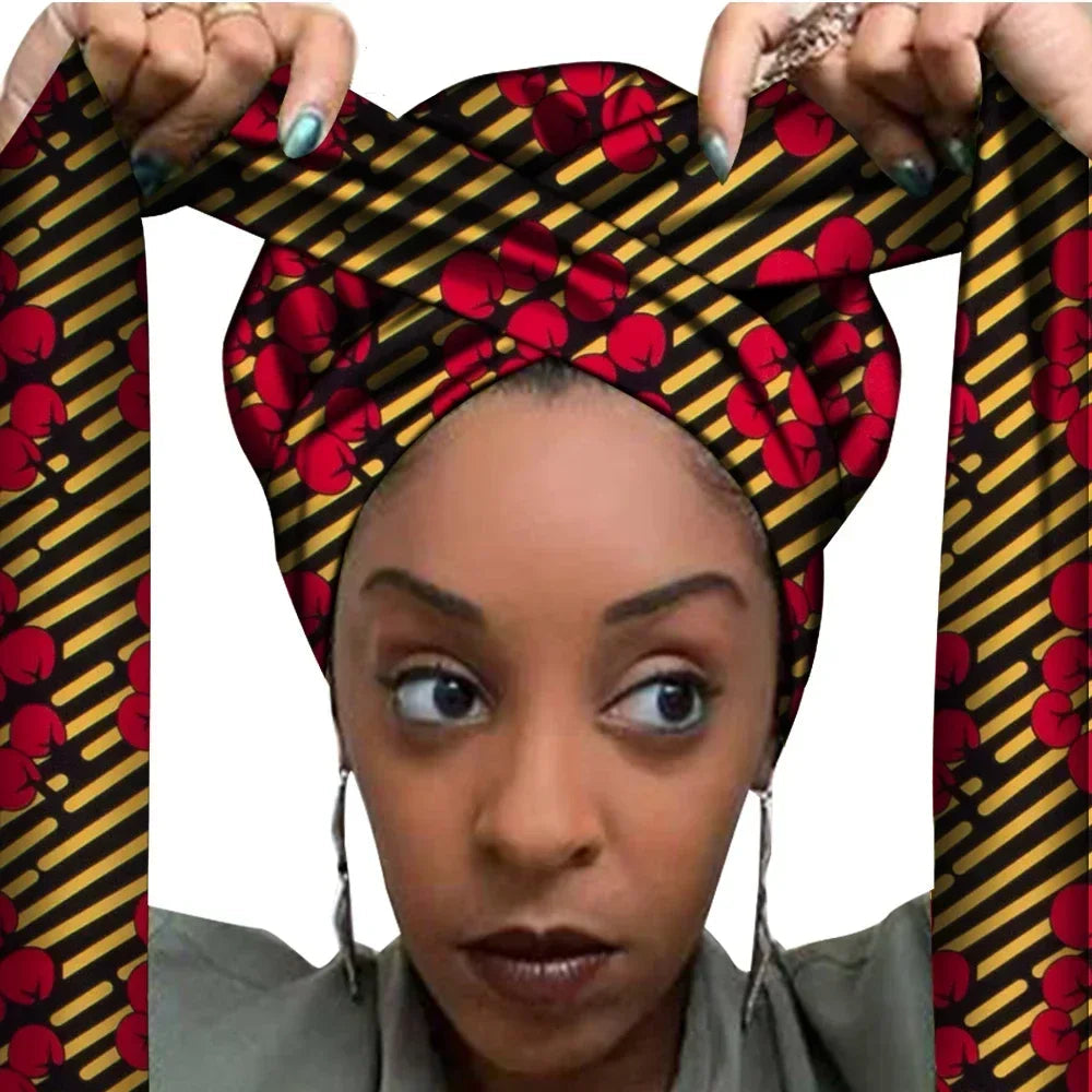 Vrouw met een Afrikaanse headwrap in zwart, geel en rood Ankara print. De stof heeft een opvallend gestreept patroon met rode bloemachtige motieven en lange linten, handgemaakt van katoen, perfect voor lente en zomer.
