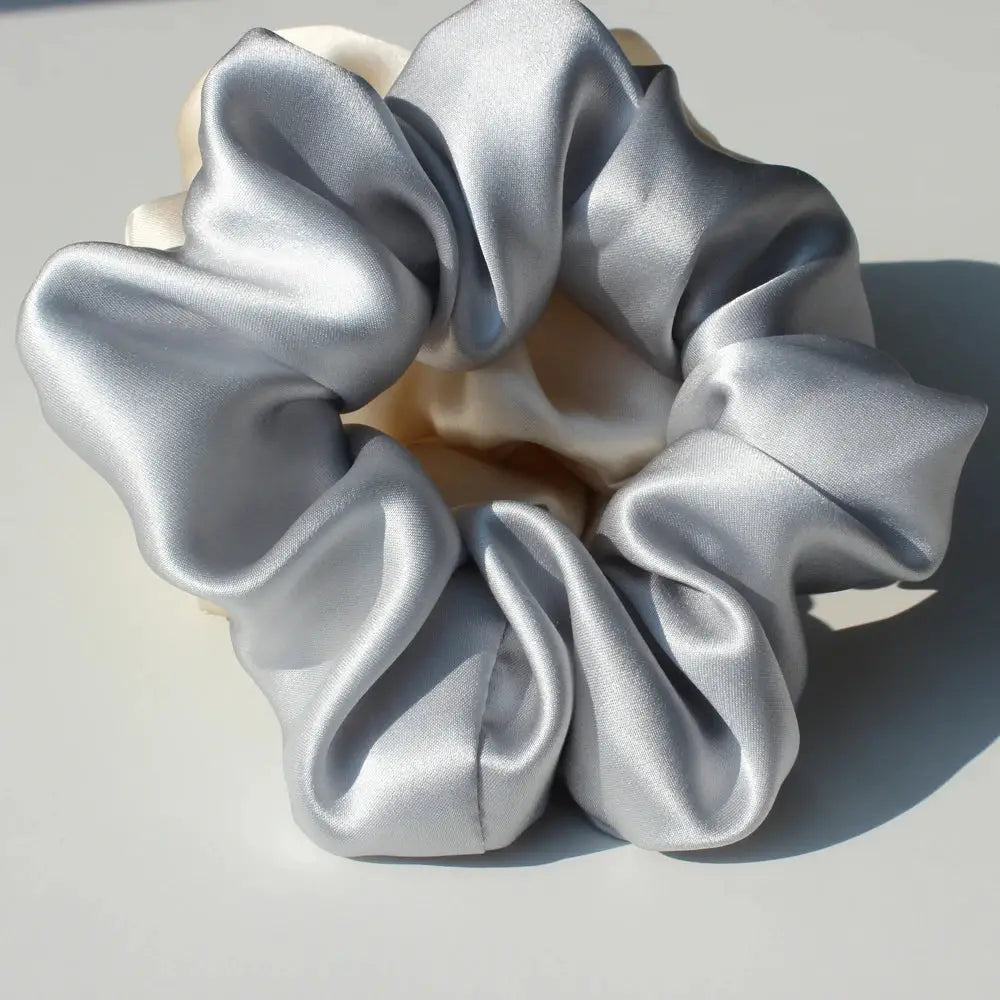 Woman wearing a silver 100% pure mulberry silk scrunchie in a low bun. Elegant and soft silk hair tie for a sleek, damage-free hairstyle.