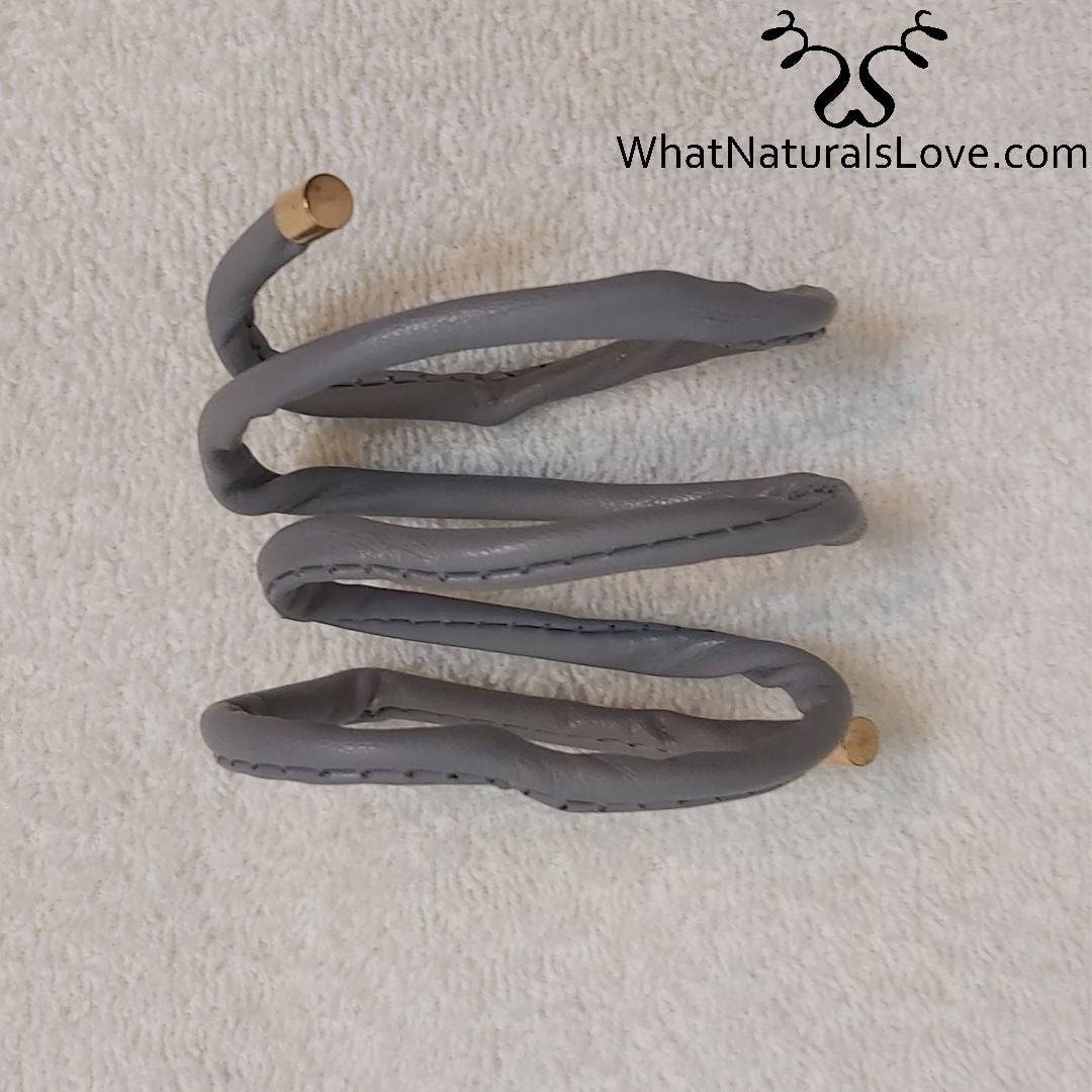 Gray non-damaging ponytail holder for locs coiled on a white surface. Ideal hair tie for dreadlocks, braids, and sisterlocks with gold-tone tips.