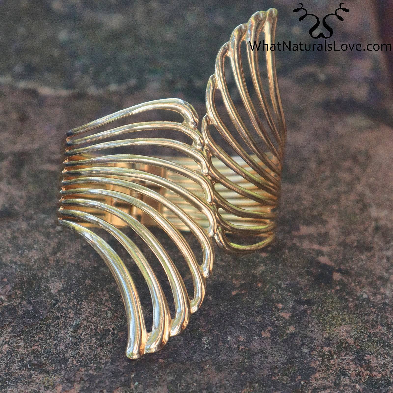 Gold Aurora Wing Cuff resting on a stone surface, showcasing its intricate wing-like structure. A fashionable hair accessory for locs and braids.