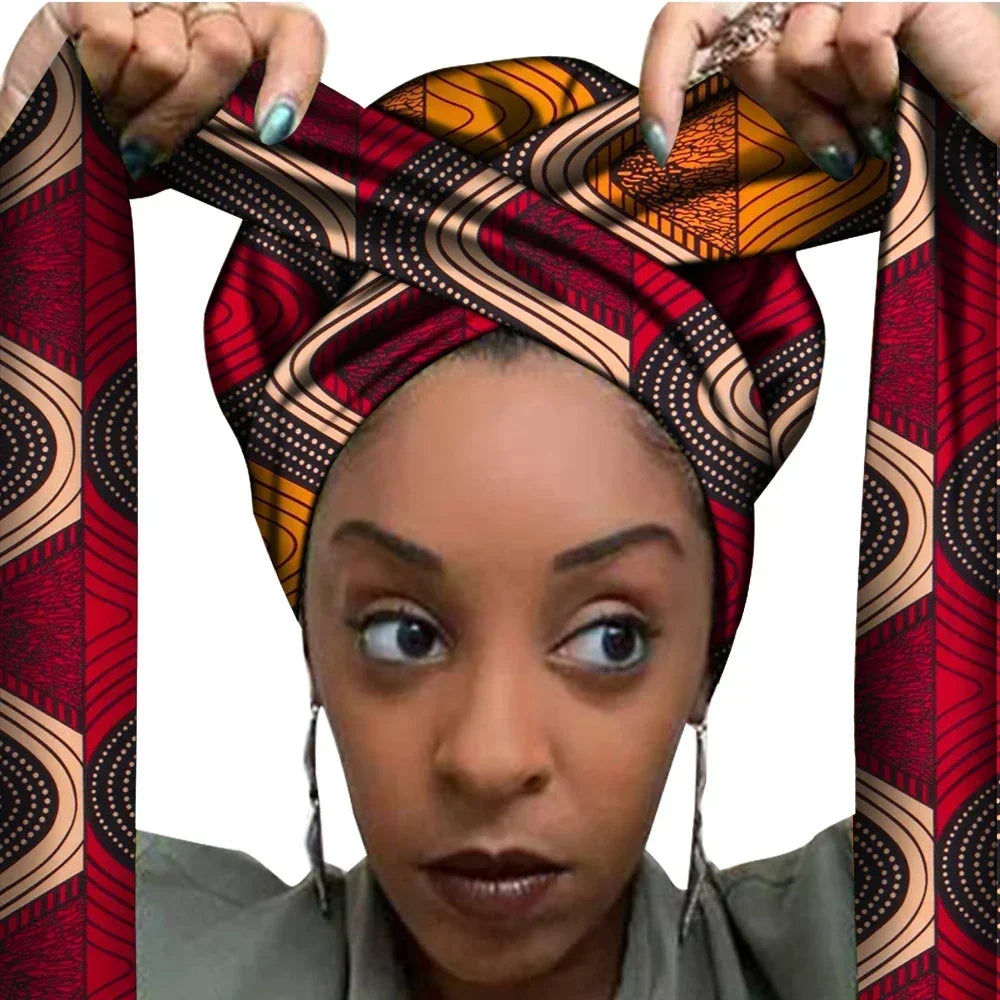 Vrouw met een Afrikaanse headwrap in rood en oranje Ankara print met beige en zwarte details. De stof heeft een geometrisch patroon met lijnen en stippen, lange linten en is handgemaakt van katoen, perfect voor lente en zomer.