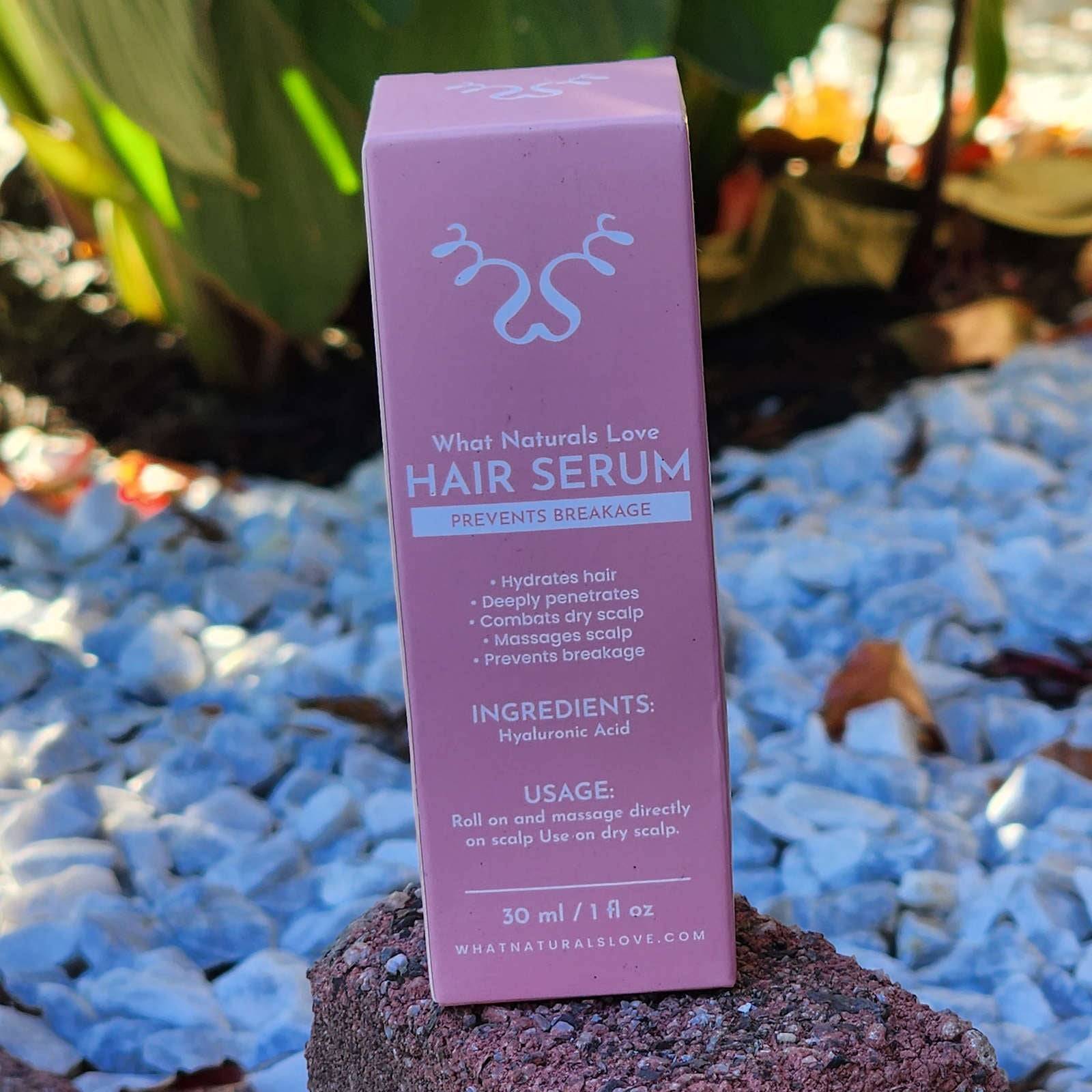 What Naturals Love Hair Serum box standing on rocks. Natural hair care serum for hydration, scalp massage, and breakage prevention.