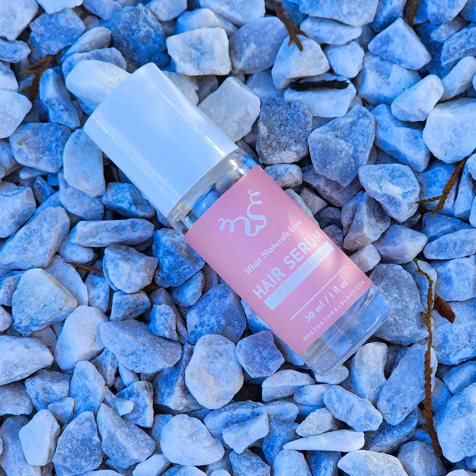 What Naturals Love Hair Serum bottle placed on decorative stones, designed to hydrate the scalp, prevent breakage, and support hair growth.