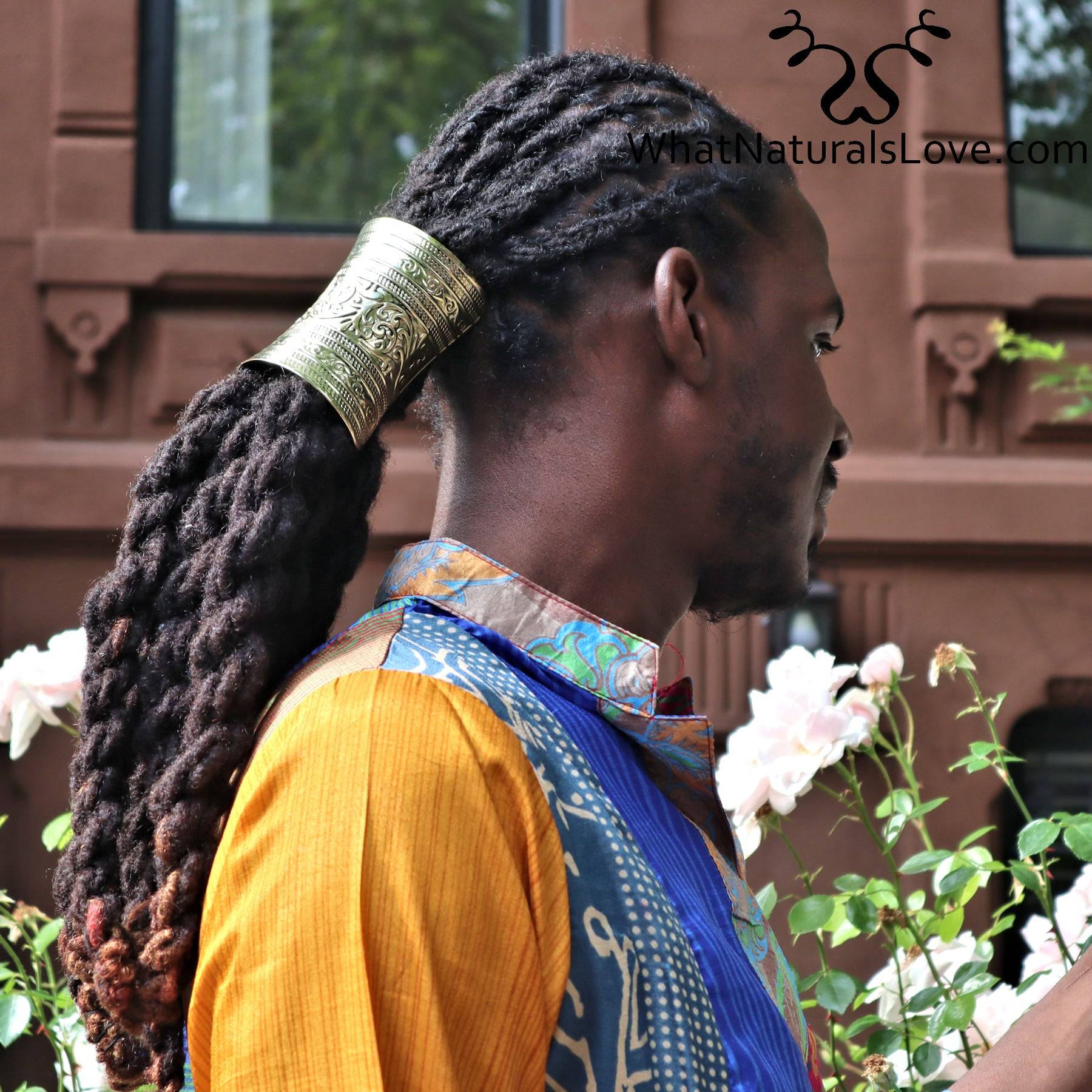 Ancient gold hair cuff securing long dreadlocks in a ponytail, worn by a man in a colorful outfit. Stylish non-damaging hair accessory for locs.