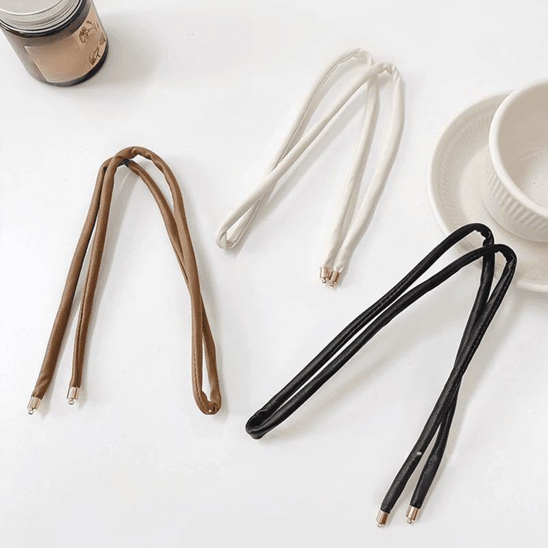 Three non-damaging ponytail holders in black, brown, and white laid on a table. Designed for securing locs, dreadlocks, braids, and sisterlocks.