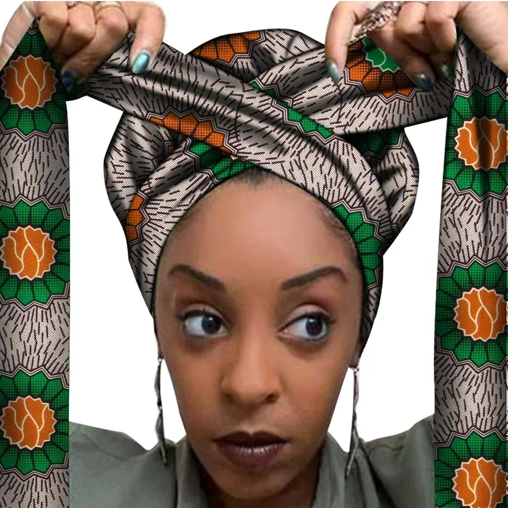 Vrouw met een Afrikaanse headwrap in beige, groen en oranje Ankara print met zwarte details. De stof heeft een bloemachtig geometrisch patroon met decoratieve lijnen, lange linten en is handgemaakt van katoen, perfect voor lente en zomer.