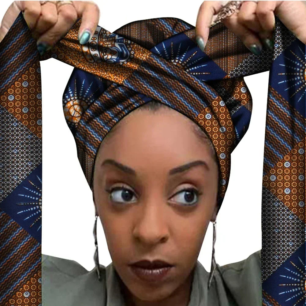 Vrouw met een Afrikaanse headwrap in donkerblauw, bruin en goud Ankara print. De stof heeft een geometrisch patroon met fijne lijnen en sterachtige vormen, lange linten en is handgemaakt van katoen, perfect voor lente en zomer.