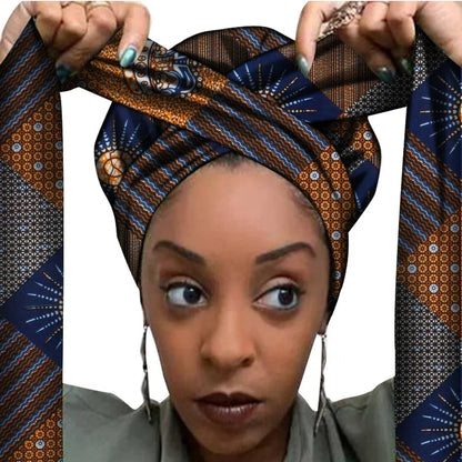 Vrouw met een Afrikaanse headwrap in donkerblauw, bruin en goud Ankara print. De stof heeft een geometrisch patroon met fijne lijnen en sterachtige vormen, lange linten en is handgemaakt van katoen, perfect voor lente en zomer.