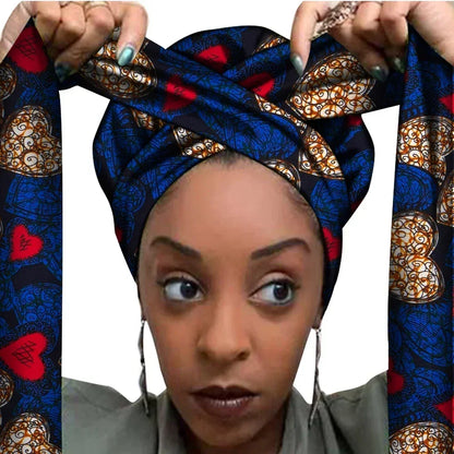 Vrouw met een Afrikaanse headwrap in donkerblauw, rood en goud Ankara print. De stof heeft een hartvormig patroon met sierlijke lijnen en accenten, lange linten en is handgemaakt van katoen, perfect voor lente en zomer.