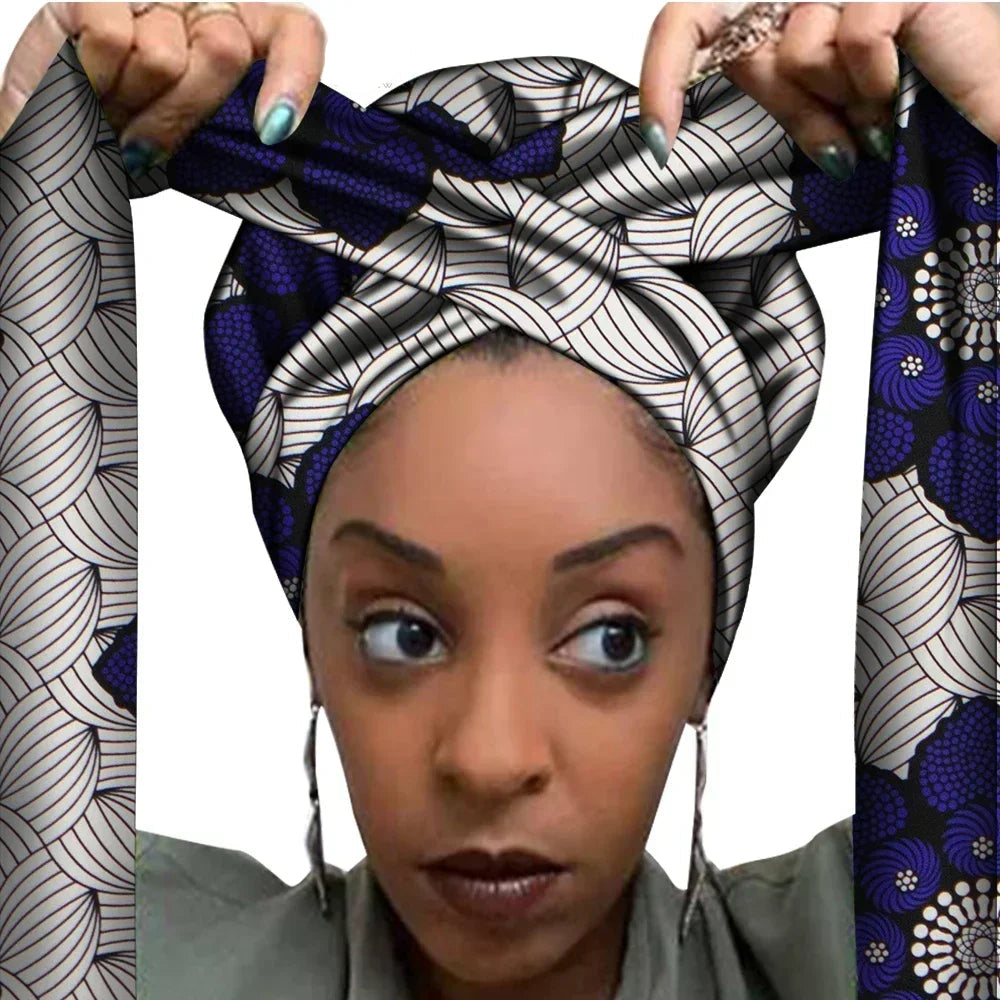 Vrouw met een Afrikaanse headwrap in donkerblauw en wit Ankara print met zwarte details. De stof heeft een opvallend blad- en bloemachtig patroon met lange linten, handgemaakt van katoen, ideaal voor lente en zomer.