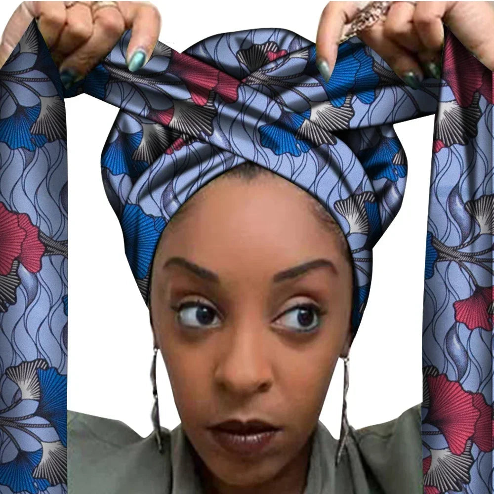 Vrouw met een Afrikaanse headwrap in grijs, blauw en bordeaux Ankara print met zwarte details. De stof heeft een elegant bloemmotief met golvende lijnen en lange linten, handgemaakt van katoen, perfect voor lente en zomer.