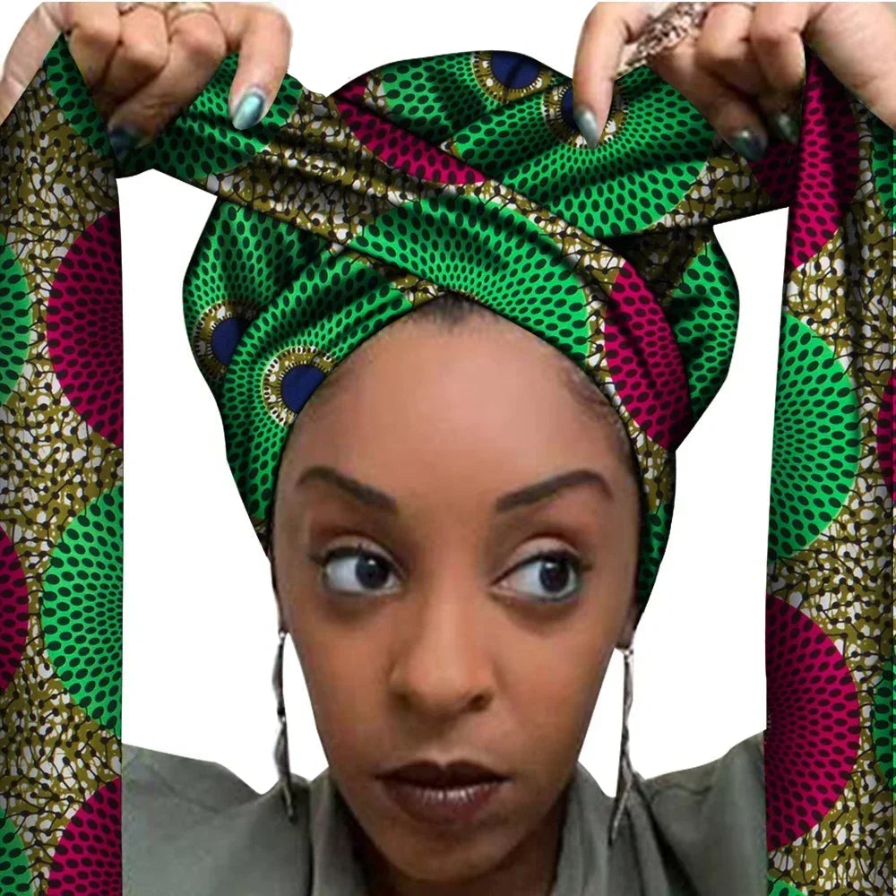 Vrouw met een Afrikaanse headwrap in groen en fuchsia Ankara print met zwarte en gouden details. De stof heeft een cirkelvormig patroon met stippen en decoratieve accenten, lange linten en is handgemaakt van katoen, perfect voor lente en zomer.
