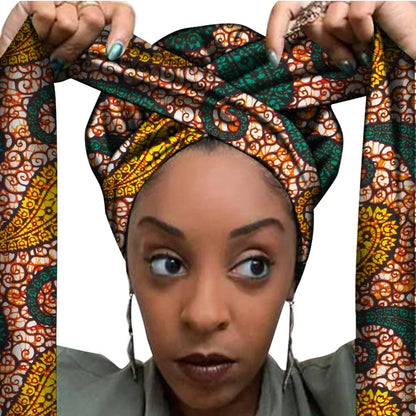 Vrouw met een Afrikaanse headwrap in groen, geel en oranje Ankara print met bruine details. De stof heeft een sierlijk, gedetailleerd patroon met krullen en bloemachtige vormen, lange linten en is handgemaakt van katoen, perfect voor lente en zomer.