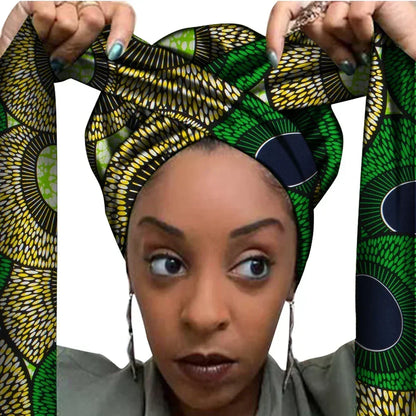 Vrouw met een Afrikaanse headwrap in groen, geel en zwart Ankara print met cirkelvormig patroon. De stof heeft een zonnebloemachtig design met lange linten, handgemaakt van katoen, perfect voor lente en zomer.