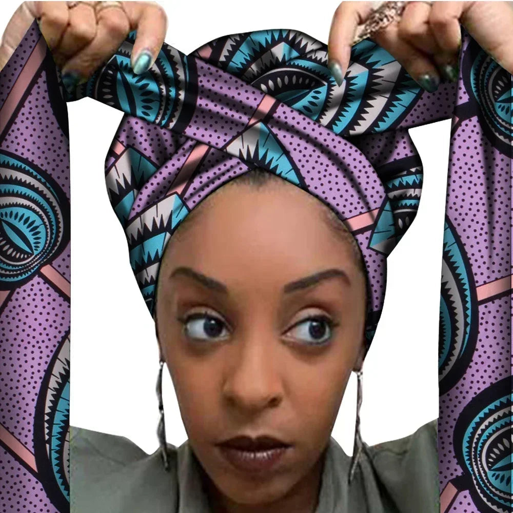 Vrouw met een Afrikaanse headwrap in lila, blauw en zwart Ankara print. De stof heeft een geometrisch patroon met driehoeken, stippen en scherpe vormen, lange linten en is handgemaakt van katoen, perfect voor lente en zomer.
