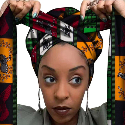Vrouw met een Afrikaanse headwrap in multicolor Ankara print met zwart, rood, groen, wit en oranje vlakken. De stof heeft een patchwork patroon met symbolen, lijnen en decoratieve figuren, lange linten en is handgemaakt van katoen, perfect voor lente en zomer.