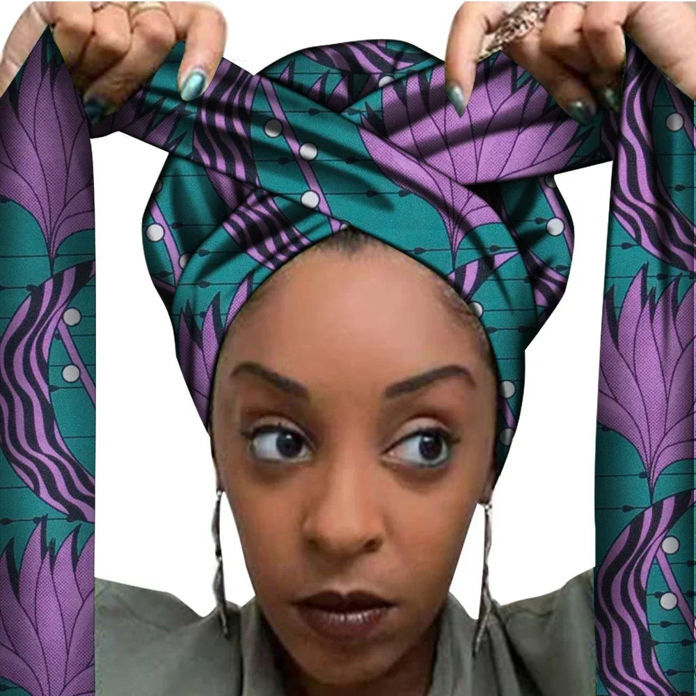 Vrouw met een Afrikaanse headwrap in paars en groen Ankara print. De stof heeft een sierlijk bladachtig patroon met fijne lijnen en stippen, lange linten en is handgemaakt van katoen, perfect voor lente en zomer.