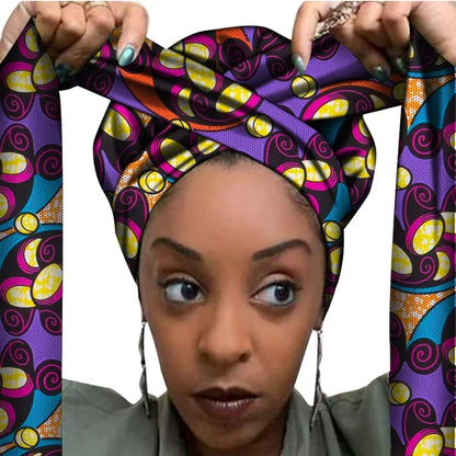 Vrouw met een Afrikaanse headwrap in paars, roze, geel en zwart Ankara print. De stof heeft een speels, golvend patroon met kleurrijke accenten en lange linten, handgemaakt van katoen, ideaal voor lente en zomer.