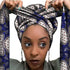 Vrouw met een Afrikaanse headwrap in wit, blauw en zwart Ankara print. De stof heeft een stervormig en decoratief geometrisch patroon met fijne details, lange linten en is handgemaakt van katoen, perfect voor lente en zomer.