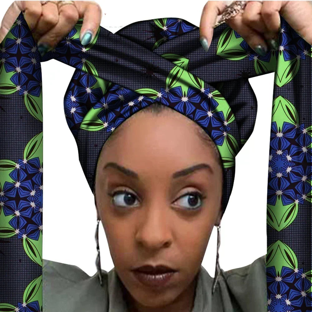 Vrouw met een Afrikaanse headwrap in groen, geel en oranje Ankara print met bruine details. De stof heeft een sierlijk, gedetailleerd patroon met krullen en bloemachtige vormen, lange linten en is handgemaakt van katoen, perfect voor lente en zomer.