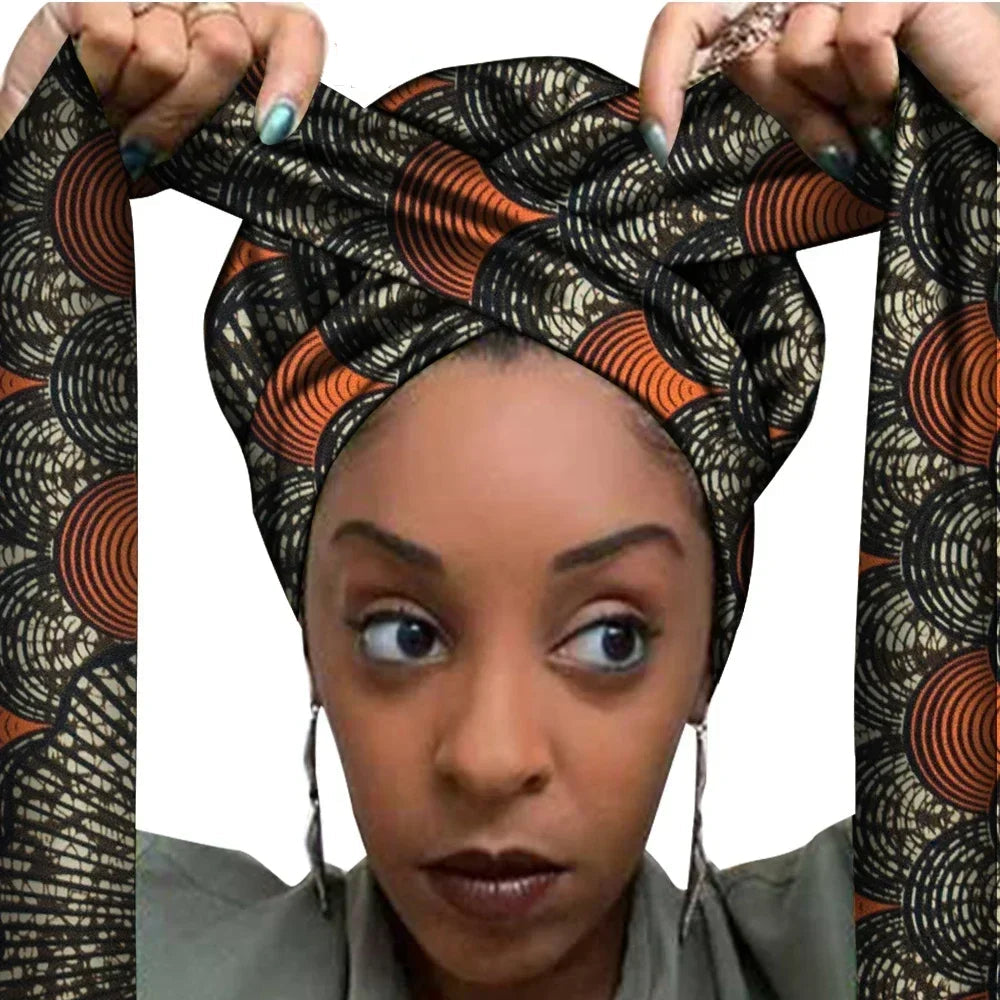 Vrouw met een Afrikaanse headwrap in zwart en oranje Ankara print met beige details. De stof heeft een cirkelvormig en grafisch patroon met lange linten, handgemaakt van katoen, ideaal voor lente en zomer.
