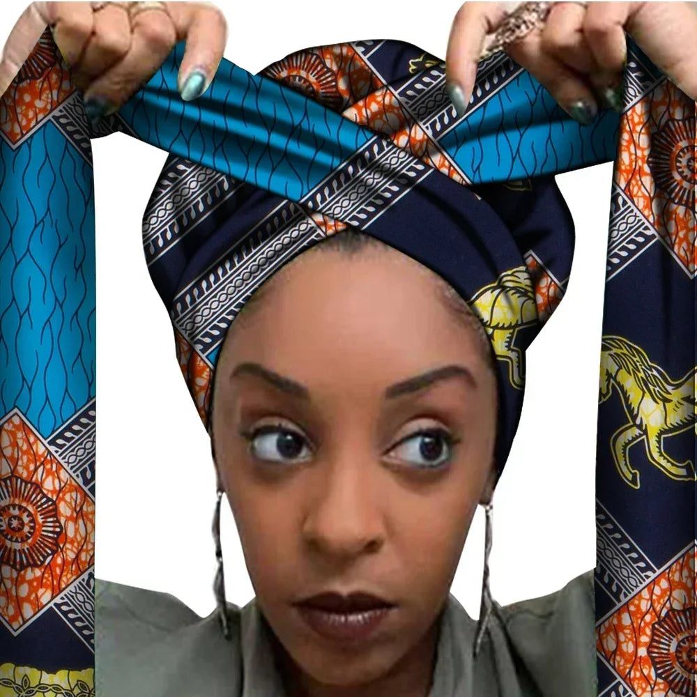 Vrouw met een Afrikaanse headwrap in blauw, oranje en zwart Ankara print met gele details. De stof heeft een geometrisch patroon met paardenmotief, decoratieve lijnen en lange linten, handgemaakt van katoen, perfect voor lente en zomer.