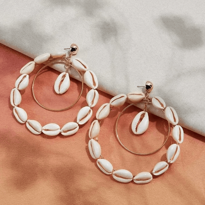 Double hoop Cowrie Shell earrings with gold-tone hoops, displayed on a gradient fabric background for an elegant presentation.