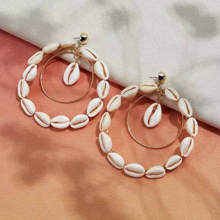 Pair of double hoop Cowrie Shell earrings with gold-tone metal hoops, displayed on a soft fabric background.