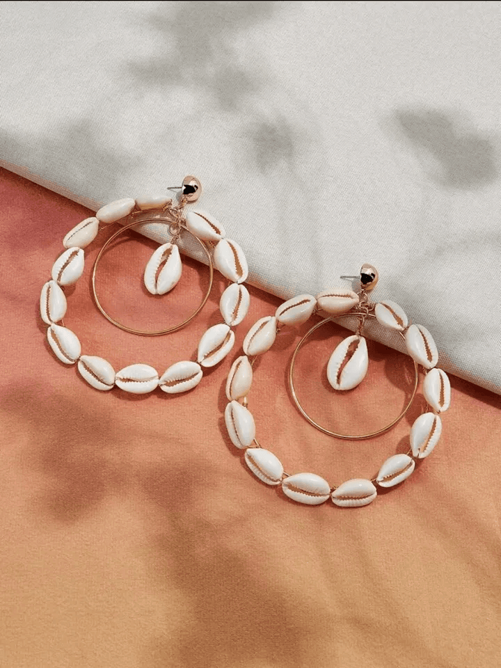 Pair of double hoop Cowrie Shell earrings with gold-tone hoops, elegantly displayed on a neutral and peach-toned fabric setting.