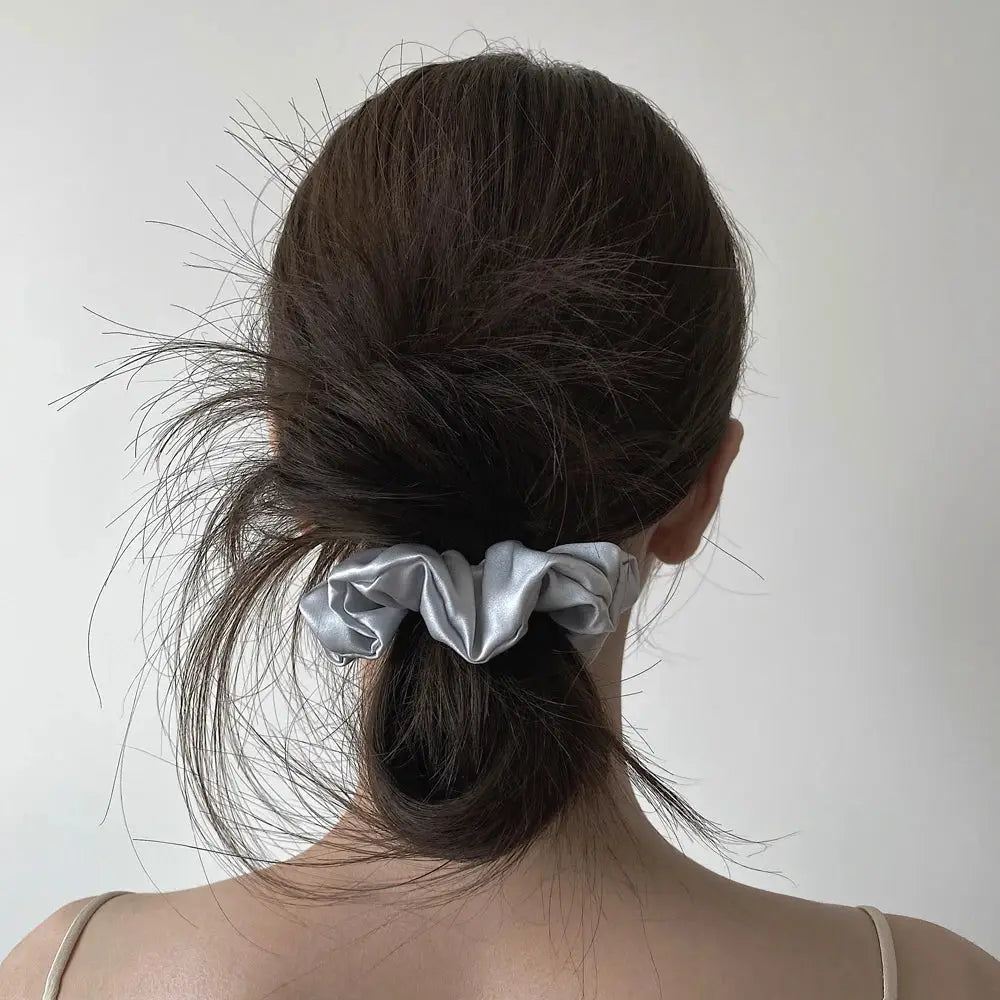 Woman styling her hair with an ivory 100% pure mulberry silk scrunchie. Gentle and smooth silk hair tie for a comfortable, crease-free hold.