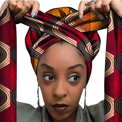 Vrouw met een Afrikaanse headwrap in rood en oranje Ankara print met beige en zwarte details. De stof heeft een geometrisch patroon met lijnen en stippen, lange linten en is handgemaakt van katoen, perfect voor lente en zomer.