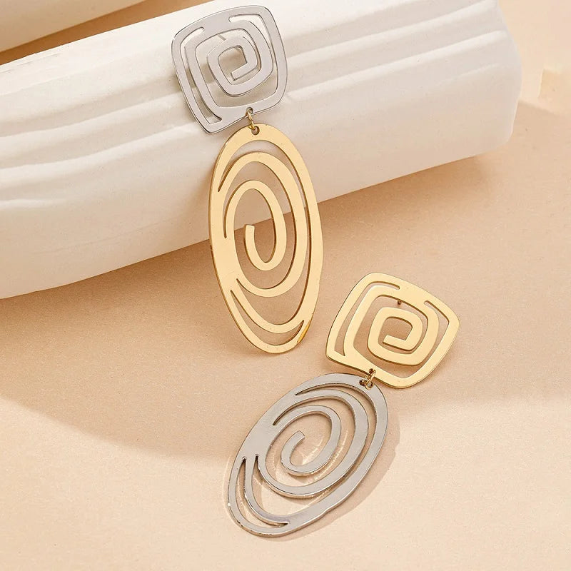 Pair of gold and silver spiral earrings on a beige surface