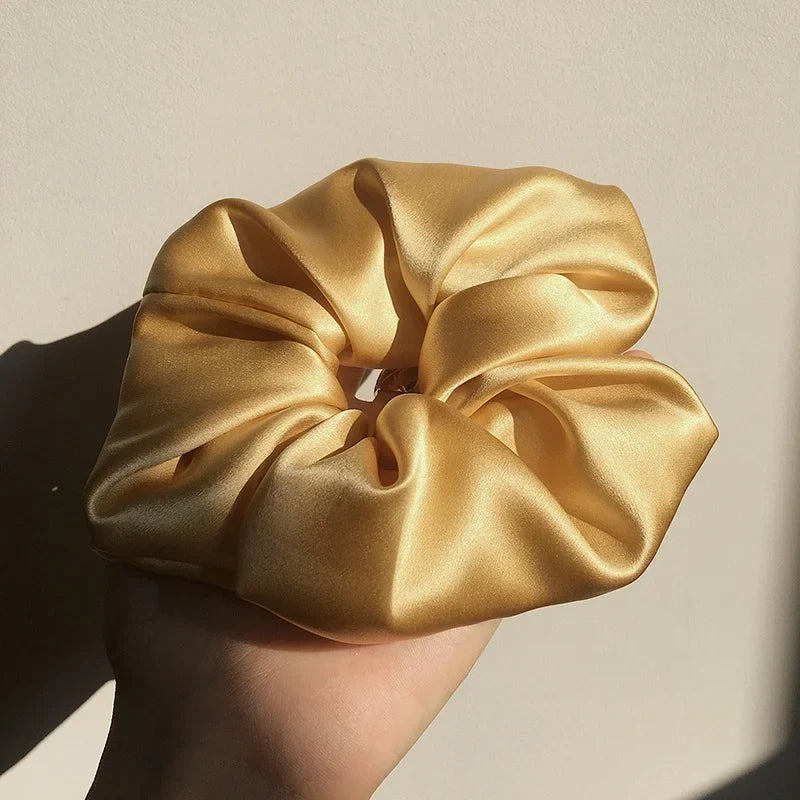 Gold silk scrunchie held by a hand against a neutral background