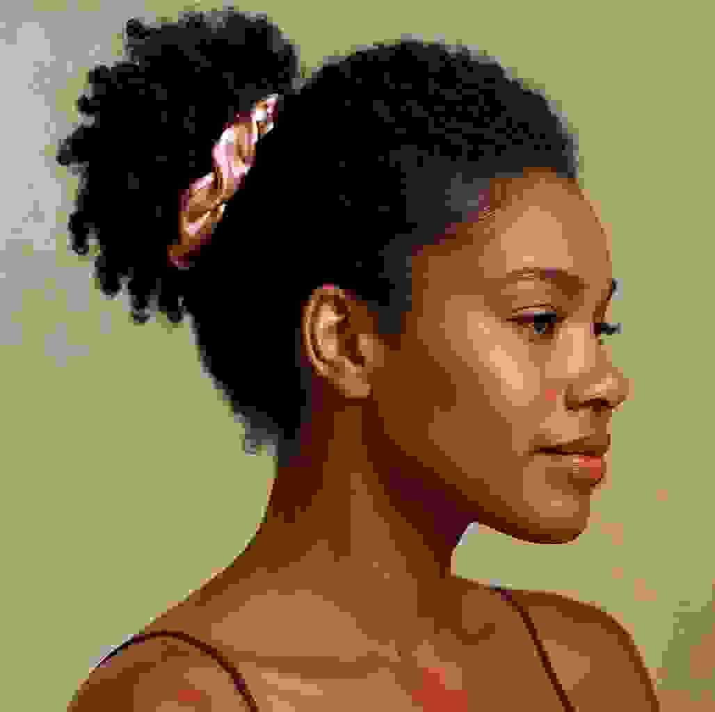 Woman with curly natural hair wearing a rose pink silk hair elastic from the Mulberry Silk Hair Elastics 8-piece set. Ideal for frizz-free styling.