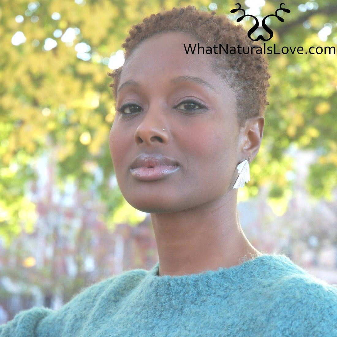 Vrouw met kort natuurlijk haar in een blauwgroene trui, met gezonde locs. De achtergrond is versierd met herfstbladeren en zacht licht.